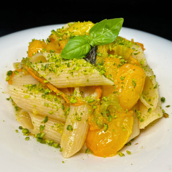 Penne Summer mit gelben Kirschtomaten, Zucchiniblüten, Basilikum und gehackten Pistazien